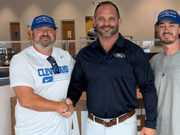 Three men shaking hands inside a Ford dealership, all smiling and wearing hats.
