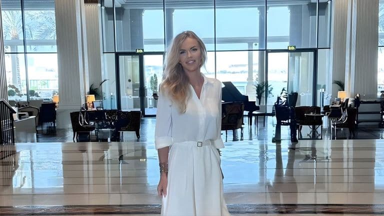 Amelia Szewczyk poses in a white dress within a stylish lobby, featuring contemporary furnishings and a welcoming atmosphere.