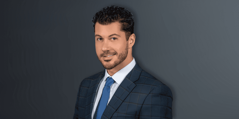 Man in a suit and tie with a stylish hairstyle against a dark background