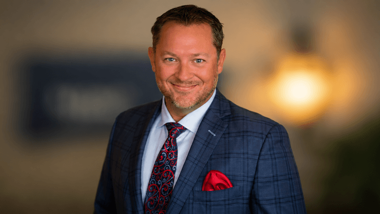 Gary Marriage Jr wearing a blue plaid suit, patterned tie, and red pocket square in a professional portrait.