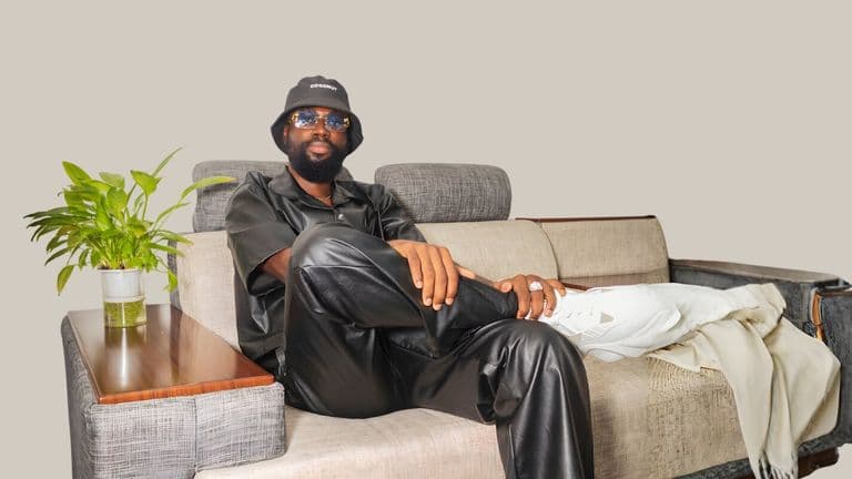 Benjamin Sarpong in stylish black leather attire, seated comfortably with one leg crossed, exuding confidence.