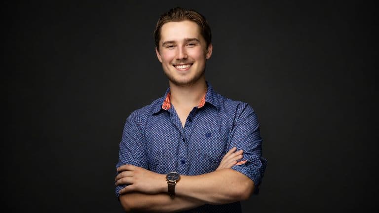 Professional portrait of Trystan Keller smiling with arms crossed against a dark background.