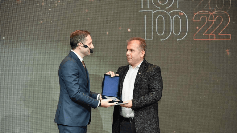 Fejsal Mustafi receiving an award during the Top 100 2022 event, with a presenter handing over the plaque.