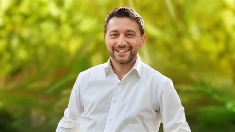 A smiling man in a white shirt stands in front of a vibrant green background, embodying positivity and confidence.