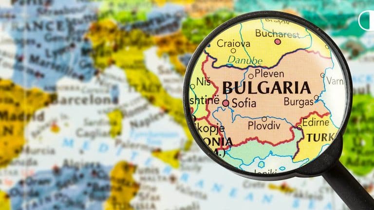 A magnifying glass highlights Bulgaria on a colorful map of Europe, showing nearby countries and the Black Sea. The focus conveys exploration and detail.