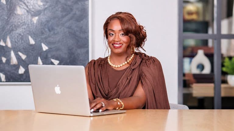 Businesswoman wearing brown attire working on laptop at conference table in contemporary office.