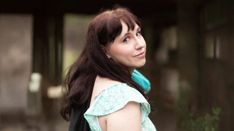 A woman with long brown hair wearing a blue scarf, looking thoughtfully into the distance.
