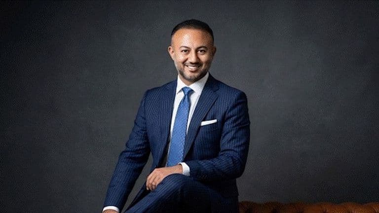 Formal portrait of Yusuf Yaran in blue suit seated against dark studio backdrop.