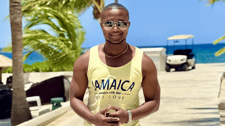 Nicholas Kerr, founder of Sales Crafter, standing in Jamaica, wearing a yellow "JAMAICA" tank top with a sunny beach backdrop.