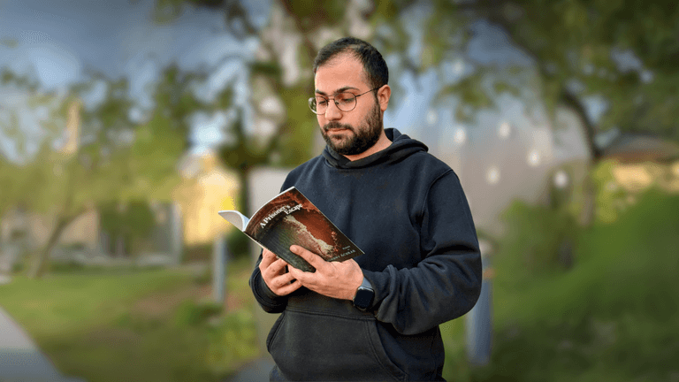 A man reading "A Prisoner's Escape" by Johnny Achkar outdoors, reflecting themes of resistance, exile, and self-reclamation.