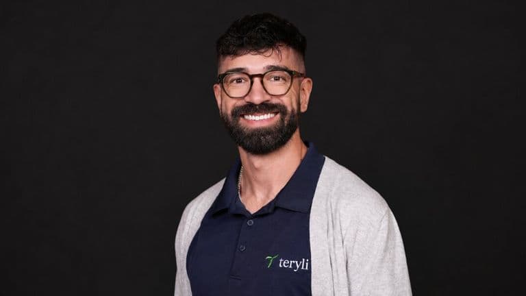 Christopher Molina wearing a Teryli polo shirt and smiling against a black studio background.