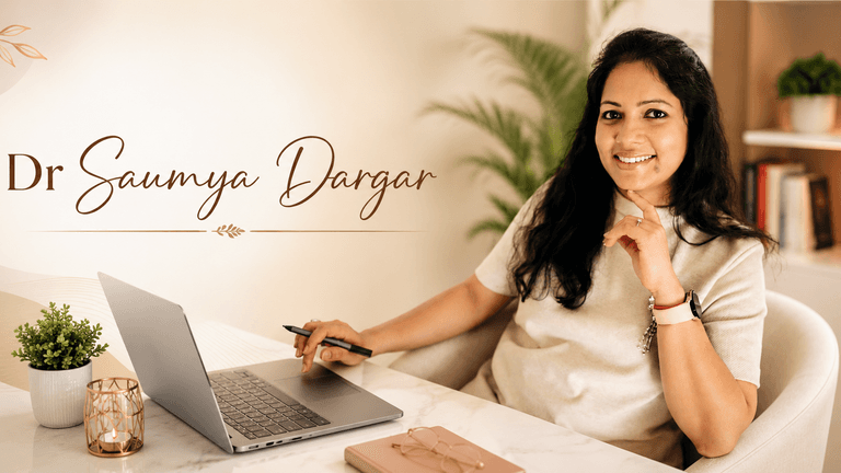Dr. Saumya Dargar smiling at a desk with laptop in a warm office, professional personal branding portrait.