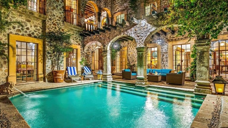 Luxury courtyard home with swimming pool, stone arches, and colonial architecture in San Miguel de Allende at night.