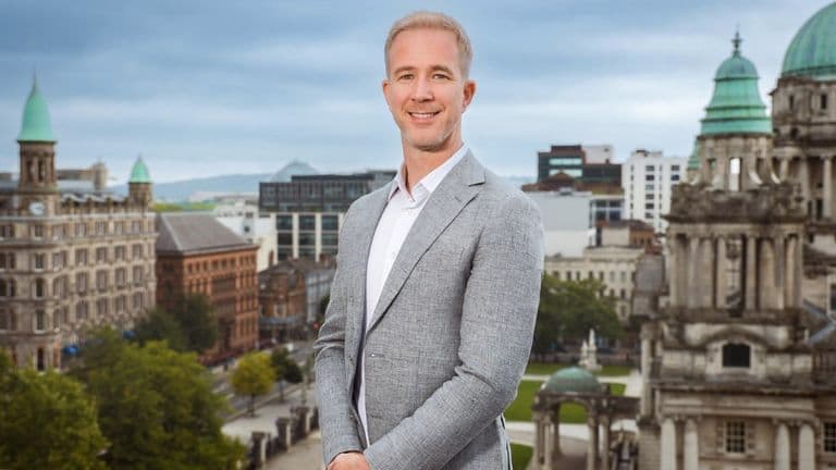 Ray Gilmour, CEO of MarketsMadeClear.com, stands confidently with the Belfast skyline behind him, symbolizing clarity in trading.