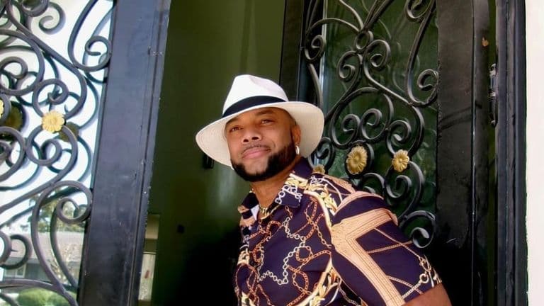 Enoch Duplechan standing confidently in a stylish shirt and hat, symbolizing leadership grounded in faith, purpose, and people.