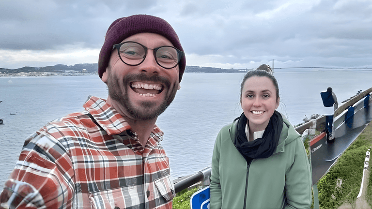 Two smiling people pose by a scenic waterfront viewpoint, representing collaborative leadership and influence from Role Model Leadership.