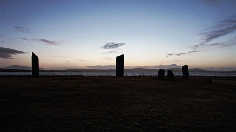 an archaeological site with standing stones against a scenic landscape, reflecting themes of historical exploration and discovery.