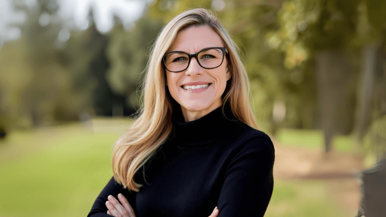 Smiling woman in black sweater and glasses standing outdoors, representing Elisha Meek’s journey from burnout to purpose.