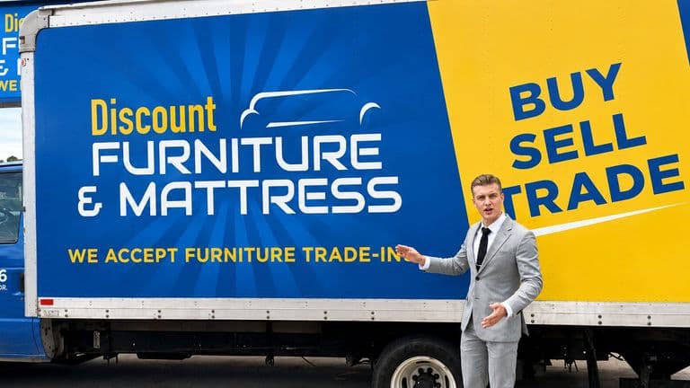 Brayden Bass standing beside a Discount Furniture & Mattress delivery truck in Surfside Beach.