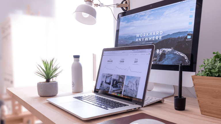 A clean, minimalist desk with a laptop and a motivational AI-related desktop background.