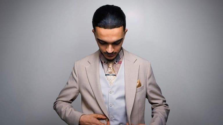 Cinen Hamila, founder of Magik Management, in a beige suit with geometric tie and golden pocket square, focused.