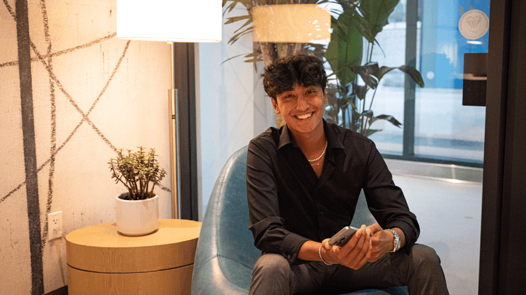 Devan Tiankee, founder of Daygency, smiles while seated in a modern office space, holding a phone.