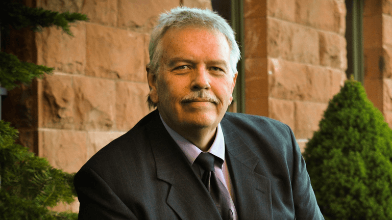 Portrait of attorney Eric Ridley in a suit, smiling outside a stone building with greenery in the background.