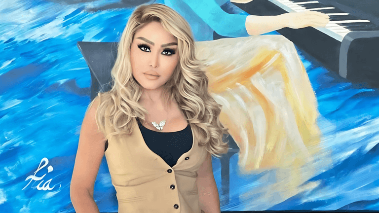 "Portrait of a woman with blonde hair standing in front of a colorful abstract painting, featuring a piano and blue tones, wearing a beige vest and a statement necklace. The painting is signed 'Lia' in white."
