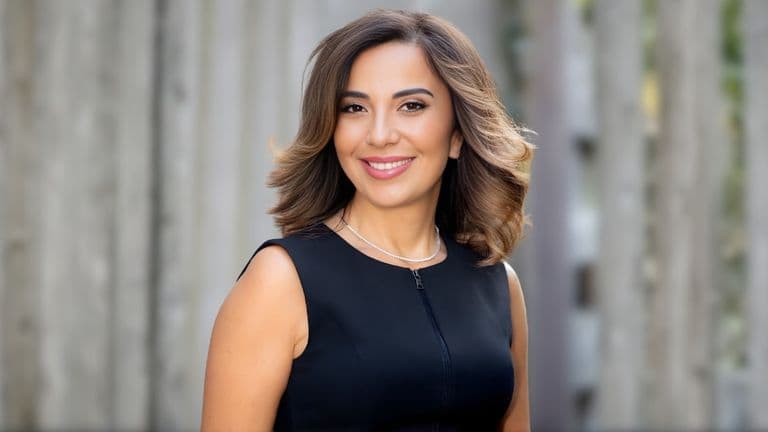 Nayla Chebli, founder of iMasterLanguages, smiling confidently in a professional black dress, with a blurred background.