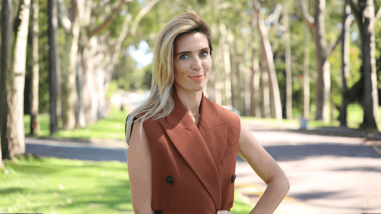 Aliya Pogorelskaya, Founder of Altinteg Technology Solutions, standing confidently outdoors in a sunlit park with a rust-brown blazer.