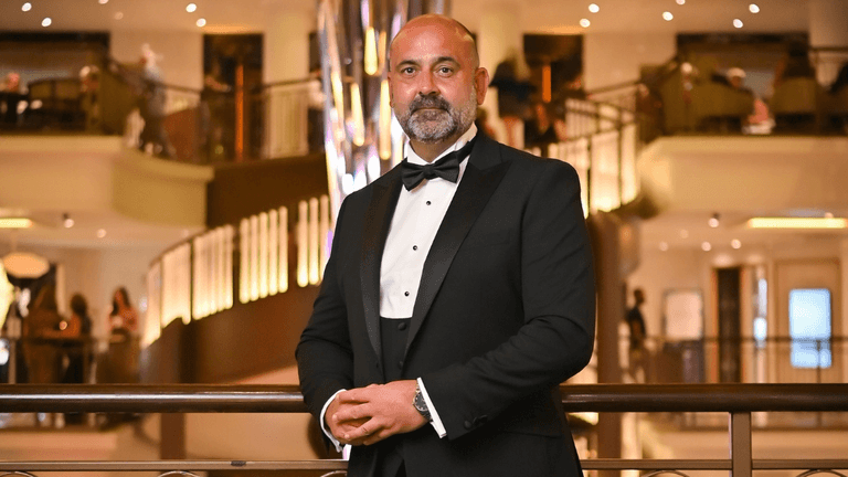 Man in black tuxedo posing confidently in an elegant hotel lobby.