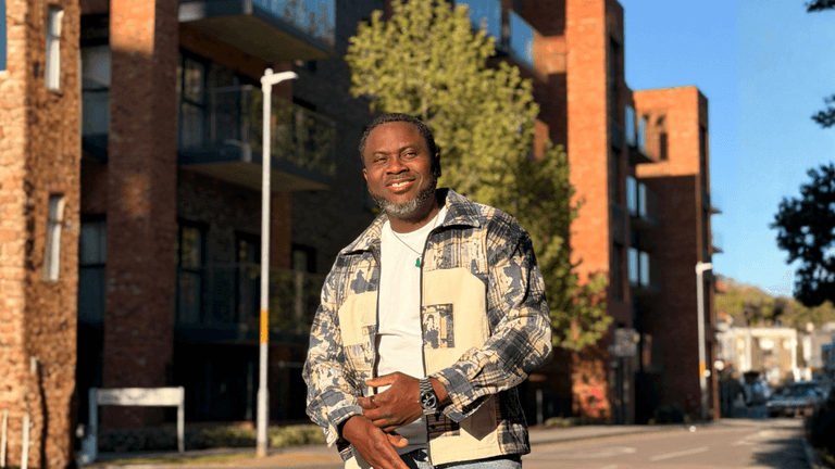 Kenny Ojo smiling outdoors in an urban neighborhood, reflecting confidence, community, and authentic storytelling.