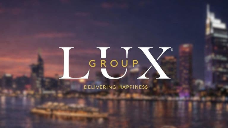 "Lux Group logo overlays a blurry city skyline at dusk, with soft lights reflecting on the water. The tagline reads 'Delivering Happiness.'"