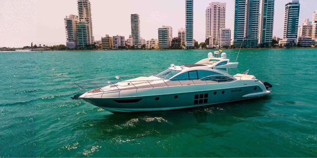 Luxury motor yacht cruising on turquoise water with Cartagena’s high-rise skyline in the background.