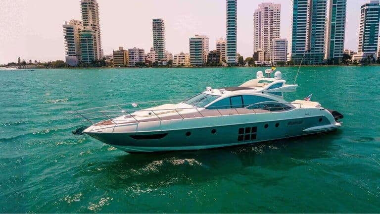 Luxury motor yacht cruising on turquoise water with Cartagena’s high-rise skyline in the background.