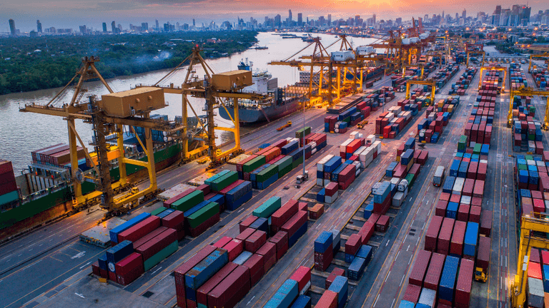 "Cargo containers and shipping cranes at a busy international port terminal during sunset, showcasing global trade, logistics, and maritime transportation infrastructure."