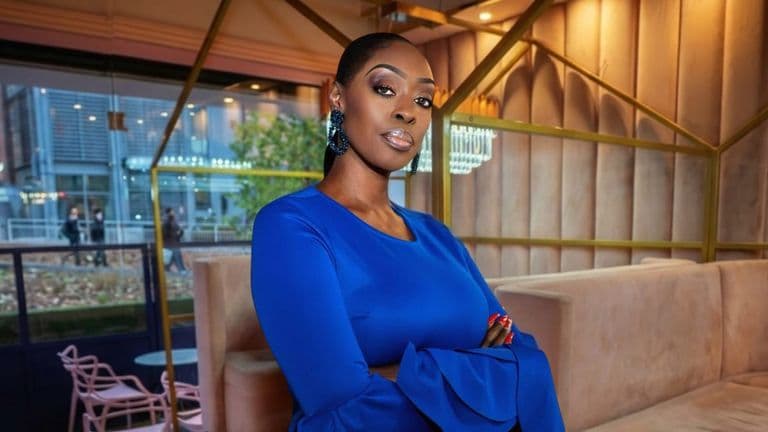 Dilys Sillah standing in a modern office wearing a blue dress with arms crossed.