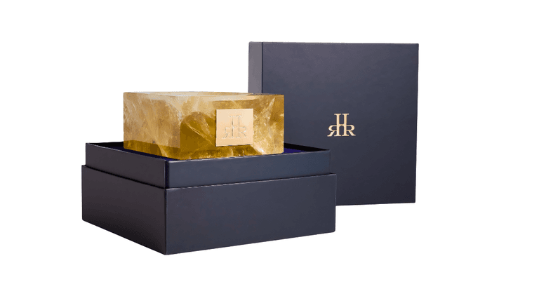 The image shows a luxurious home fragrance candle by RHR Luxury, encased in a gold crystal vessel, symbolizing artisanal craftsmanship and premium design.