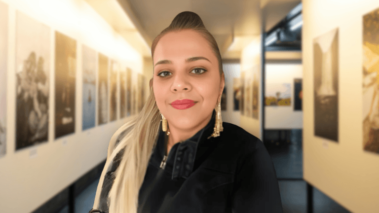 Woman smiling in an art gallery hallway lined with large, framed photographs on both walls.