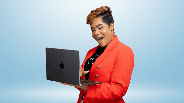 Woman in a red blazer happily using a laptop with a bright blue background, displaying enthusiasm and engagement.