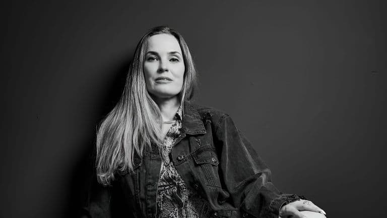 Black-and-white portrait of woman in denim jacket against a plain wall.