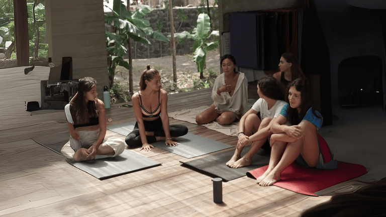 A group of women practicing yoga together in a serene indoor space surrounded by lush greenery, focusing on mindfulness and well-being
