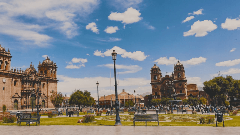 Plaza de Armas in Cusco, Peru, with historic churches and vibrant crowds under a bright blue sky.