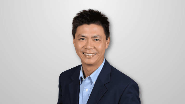 Headshot of a smiling man in a blue blazer, with short hair and a professional demeanor, set against a white background.