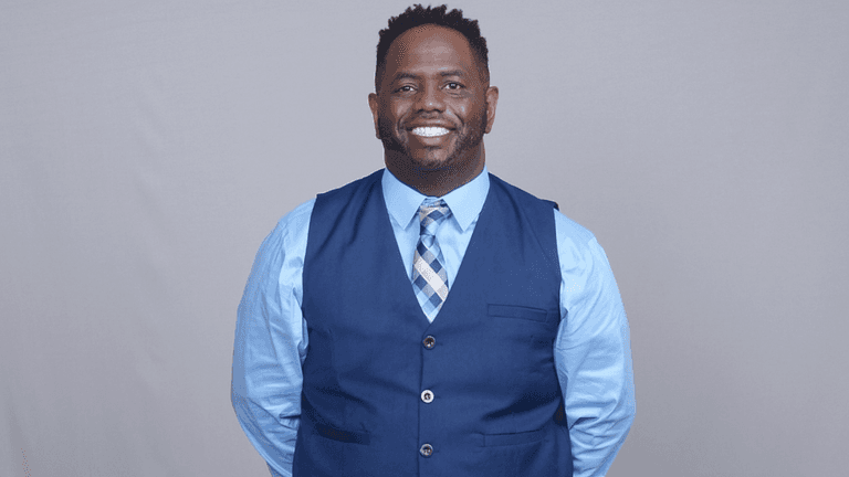 Rashad Woods smiling in a blue vest and tie, founder of The T.R.O.N. Podcast promoting meaningful global conversations.