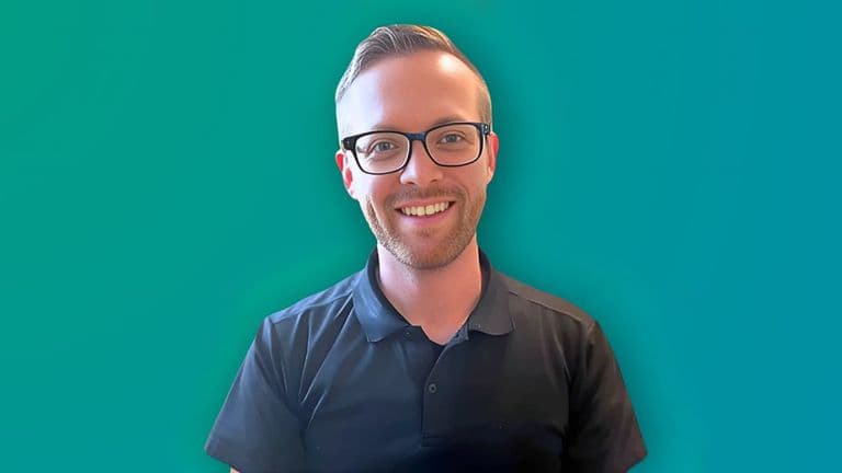 Portrait of a smiling man wearing glasses and a black polo shirt, standing against a vibrant teal background.