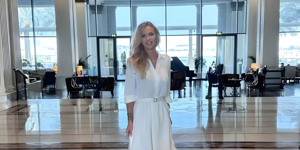 Amelia Szewczyk poses in a white dress within a stylish lobby, featuring contemporary furnishings and a welcoming atmosphere.