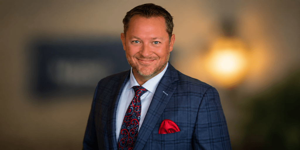 Gary Marriage Jr wearing a blue plaid suit, patterned tie, and red pocket square in a professional portrait.