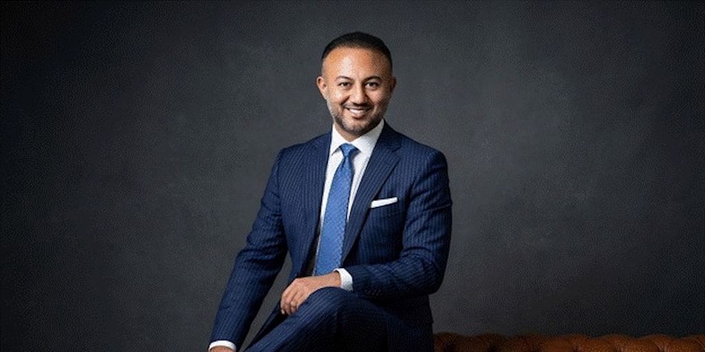 Formal portrait of Yusuf Yaran in blue suit seated against dark studio backdrop.