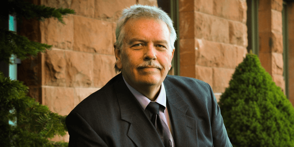Portrait of attorney Eric Ridley in a suit, smiling outside a stone building with greenery in the background.